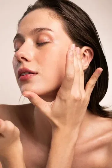 Mulher de olhos fechados aplicando sérum no rosto