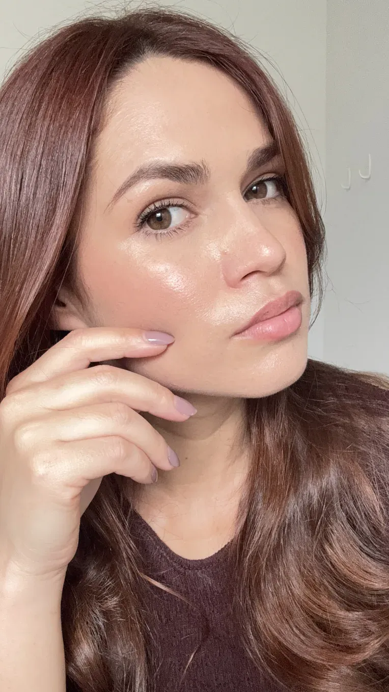 Mulher com a pele luminosa e uniforme, com a mão apoiada no rosto