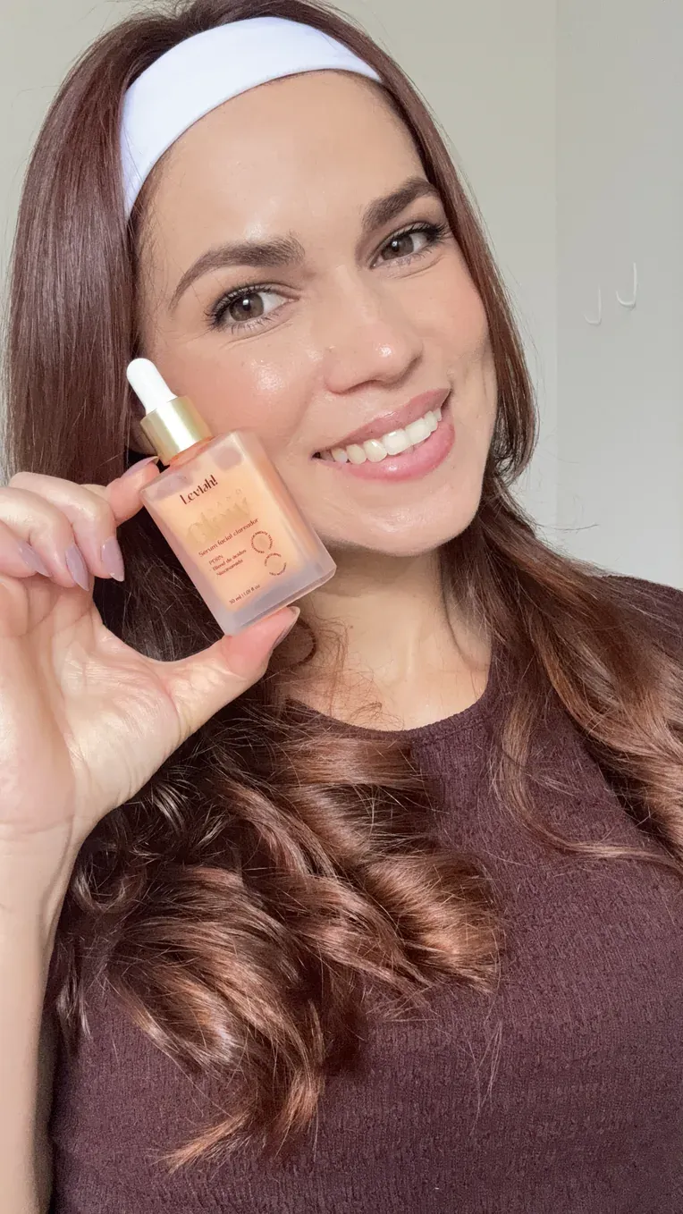 Mulher sorrindo com a pele luminosa, segurando o frasco do NanoGlow
