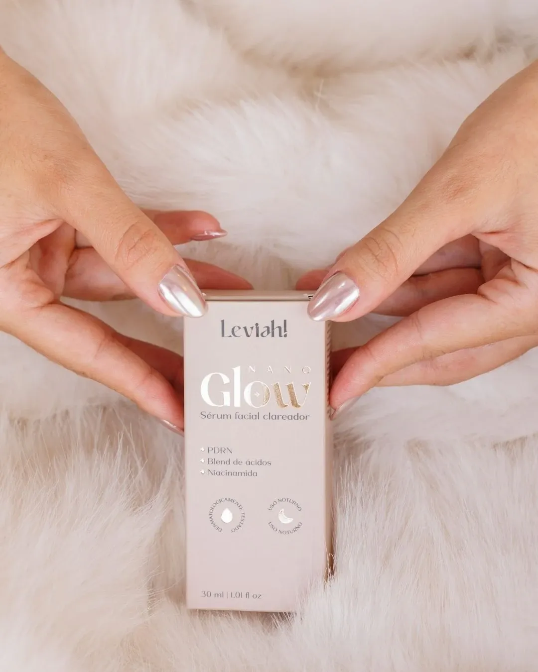 Mãos segurando a caixa do sérum NanoGlow sobre pelo branco
