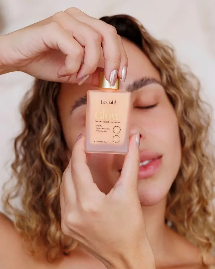 Mulher de olhos fechados segurando o frasco do sérum NanoGlow em frente ao rosto